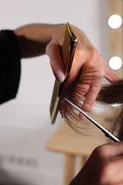 Hairdresser cutting client's hair with scissors in salon, closeup