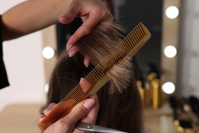 Photo of Hairdresser combing woman's hair in salon, closeup