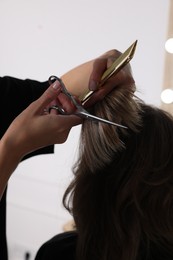 Hairdresser cutting client's hair with scissors in salon, closeup