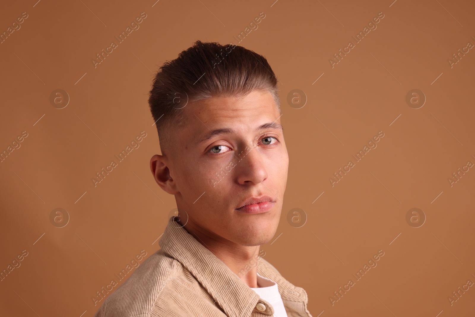 Photo of Confident young man with stylish haircut on brown background