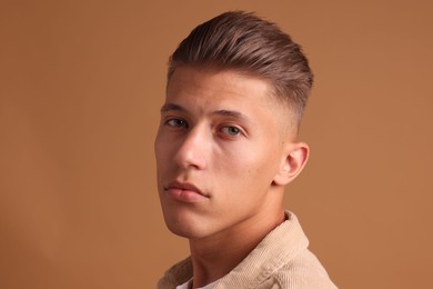 Photo of Confident young man with stylish haircut on brown background