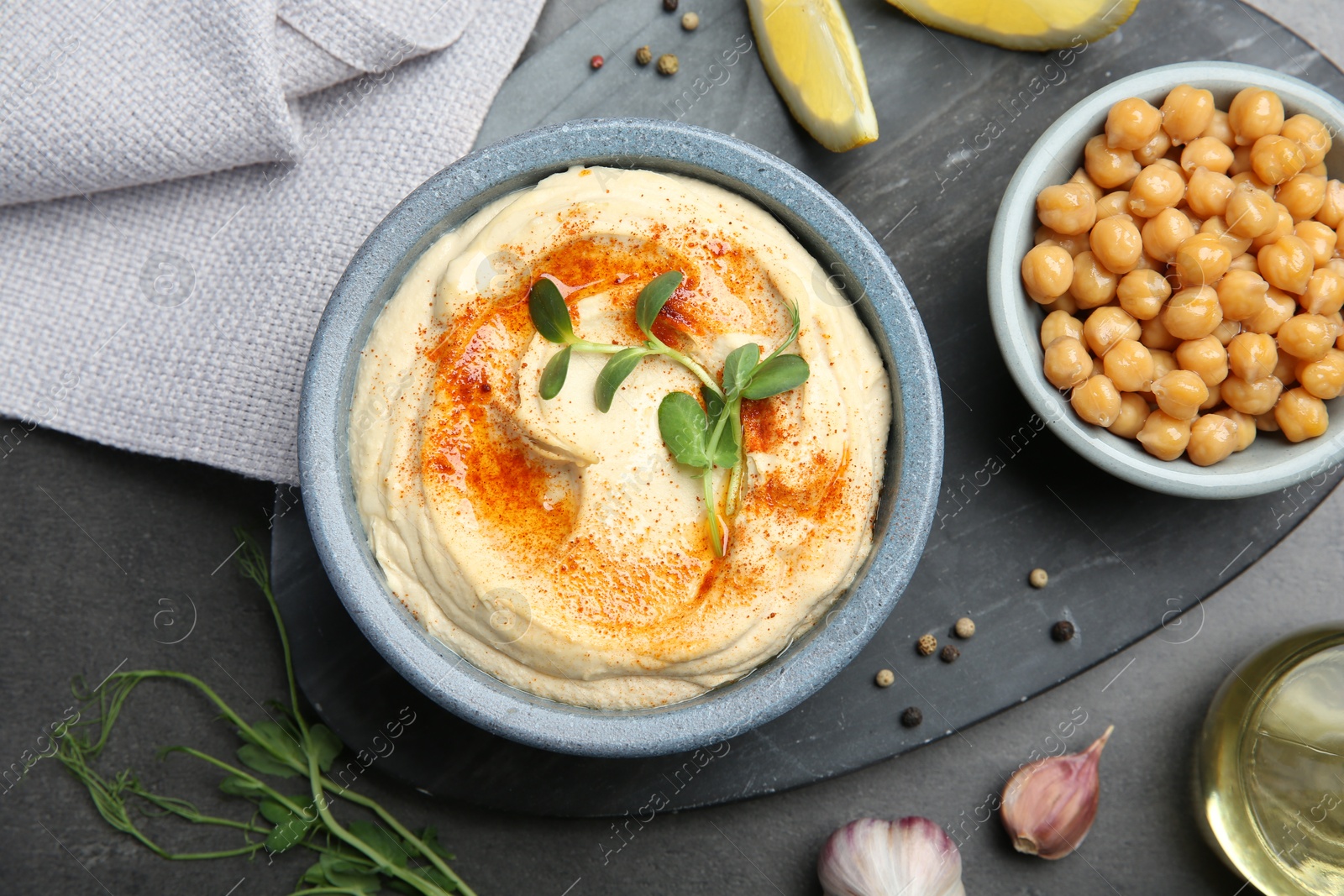 Photo of Delicious hummus with paprika and chickpeas served on dark grey table, flat lay.