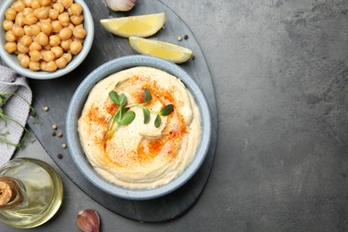 Photo of Delicious hummus with paprika and chickpeas served on dark grey table, flat lay. Space for text