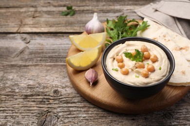 Photo of Delicious hummus with chickpeas and pita served on wooden table, space for text