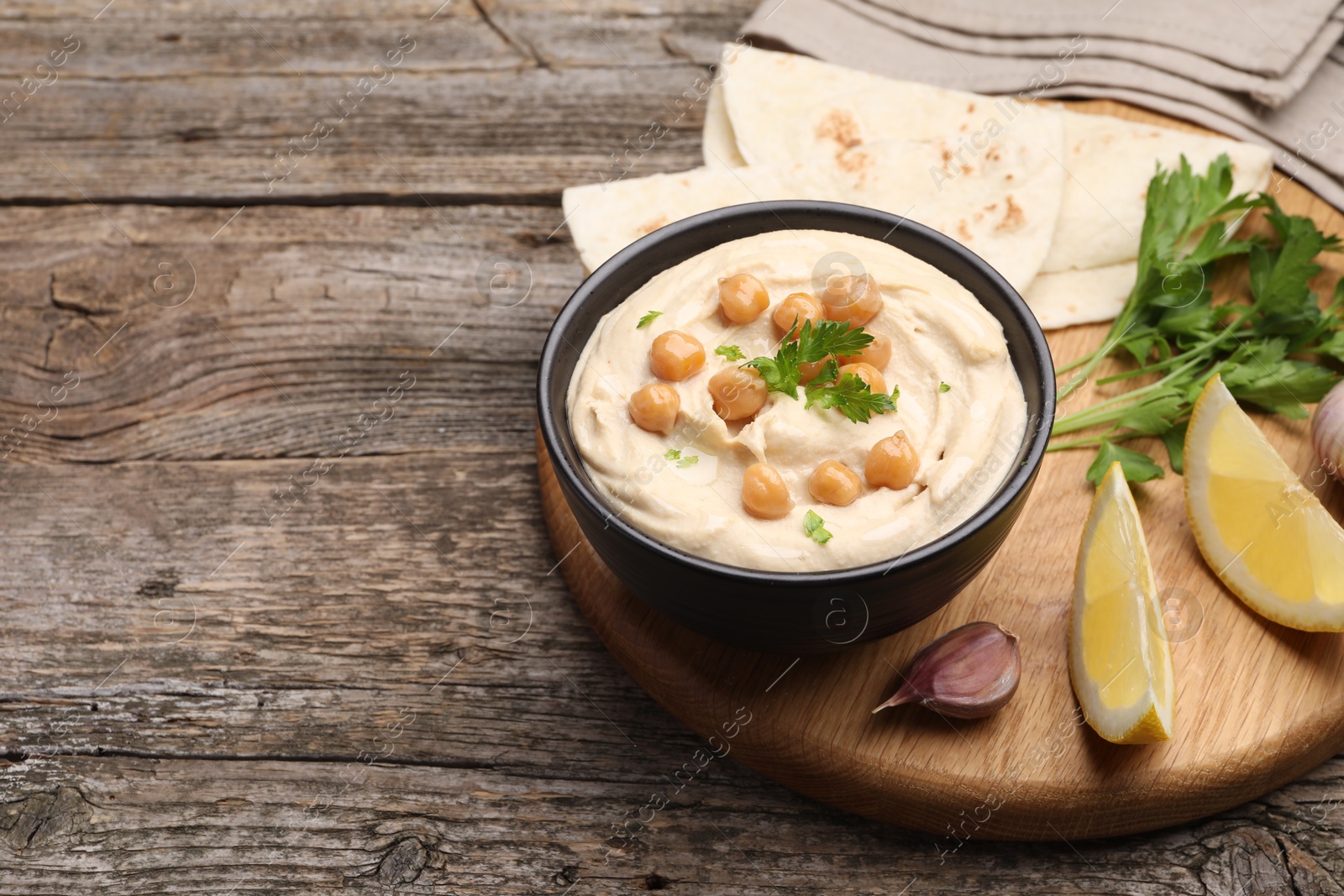 Photo of Delicious hummus with chickpeas and pita served on wooden table, space for text