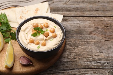 Photo of Delicious hummus with chickpeas and pita served on wooden table, space for text