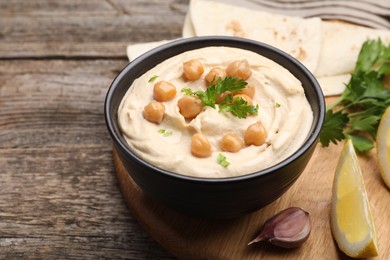 Photo of Delicious hummus with chickpeas and pita served on wooden table