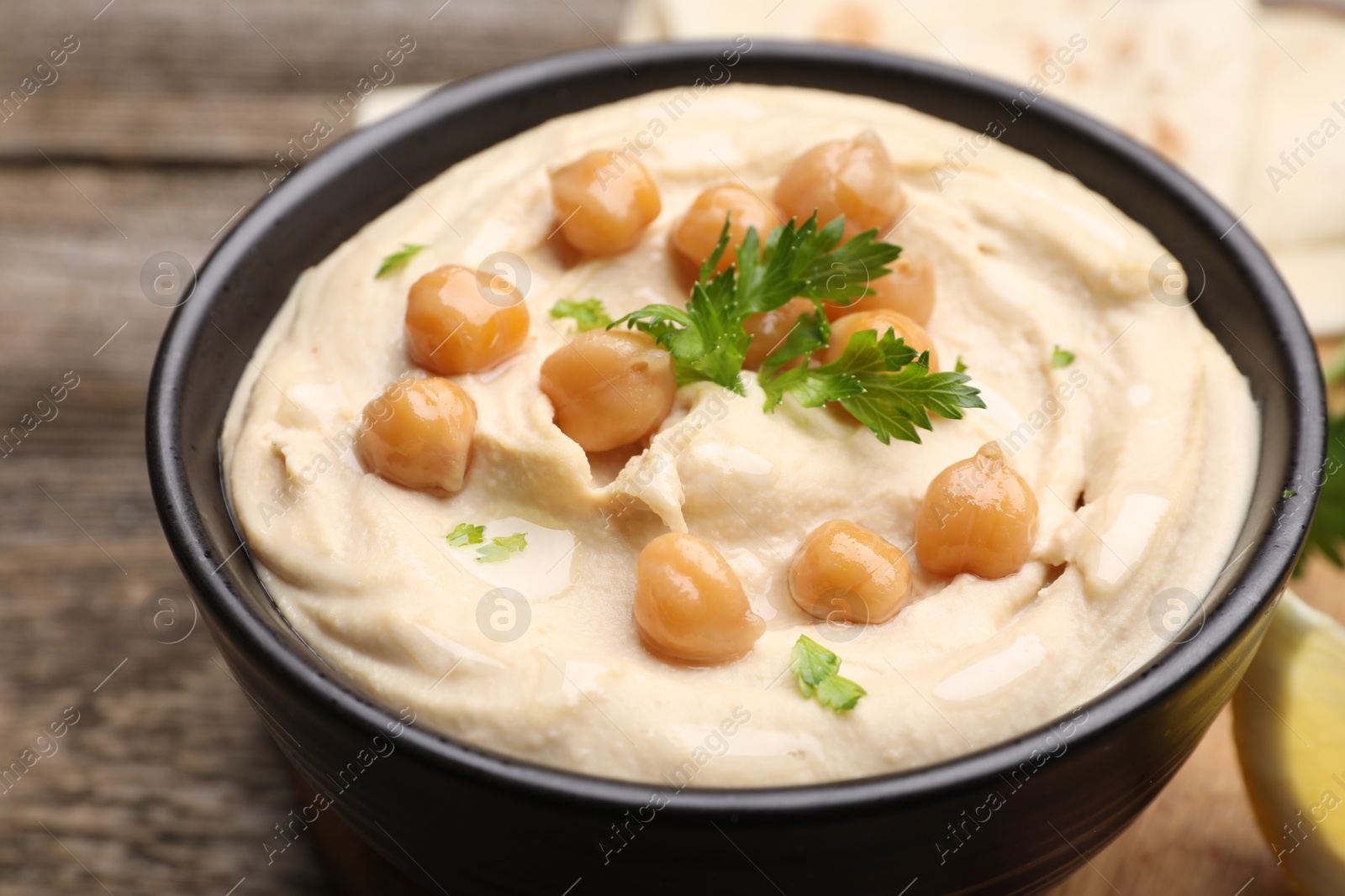 Photo of Delicious hummus with chickpeas and pita served on wooden table, closeup