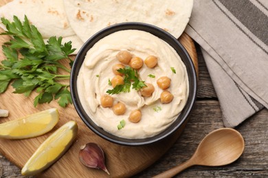 Photo of Delicious hummus with chickpeas and pita served on wooden table, flat lay