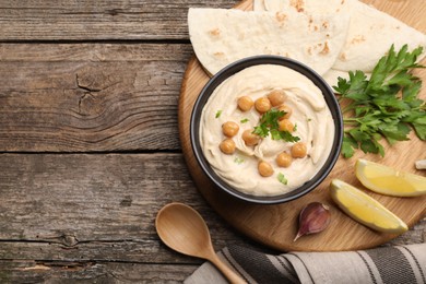 Photo of Delicious hummus with chickpeas and pita served on wooden table, flat lay. Space for text