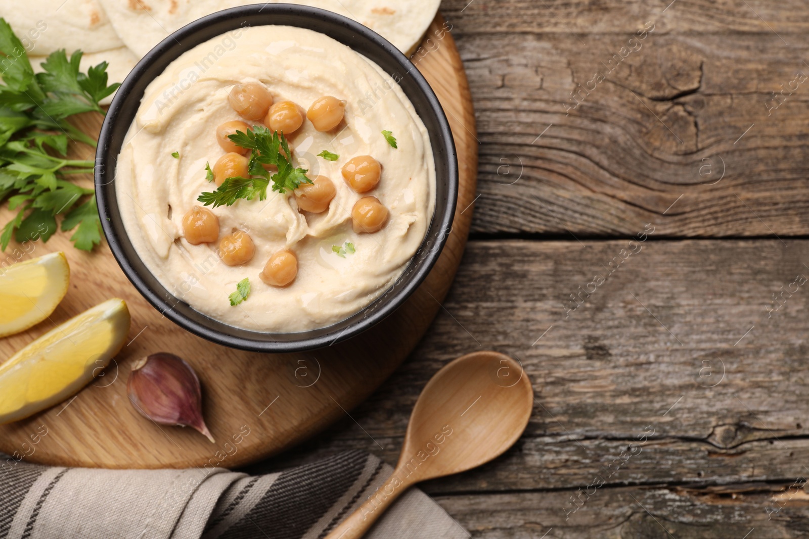 Photo of Delicious hummus with chickpeas and pita served on wooden table, flat lay. Space for text