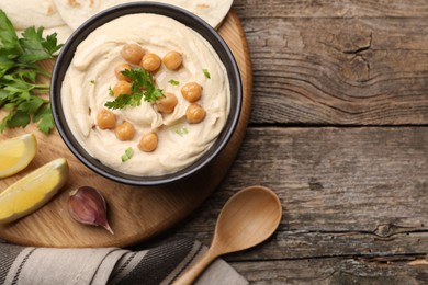 Photo of Delicious hummus with chickpeas and pita served on wooden table, flat lay. Space for text