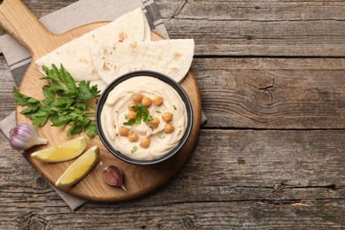 Delicious hummus with chickpeas and pita served on wooden table, flat lay. Space for text