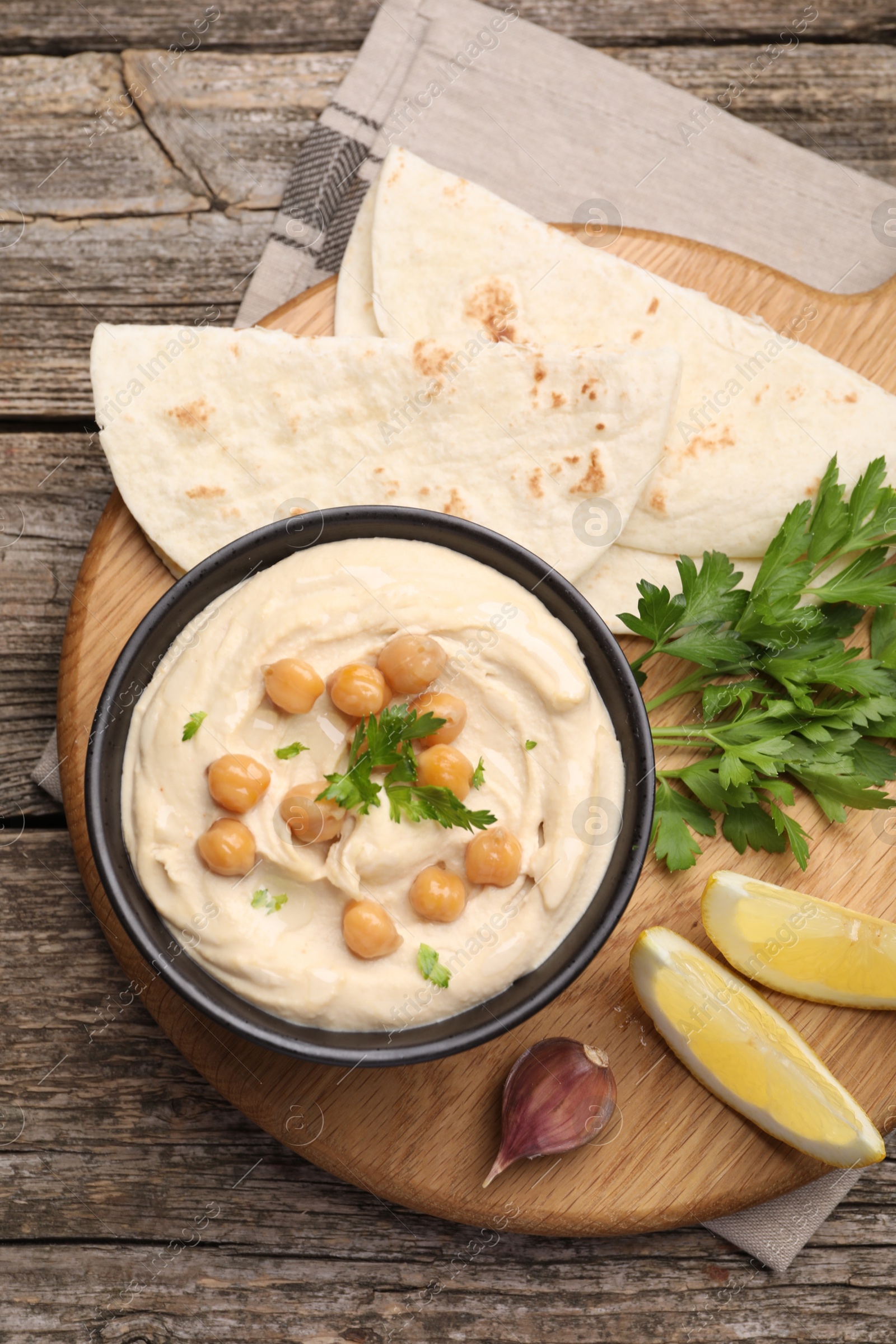 Photo of Delicious hummus with chickpeas and pita served on wooden table, flat lay