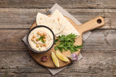 Photo of Delicious hummus with chickpeas and pita served on wooden table, flat lay