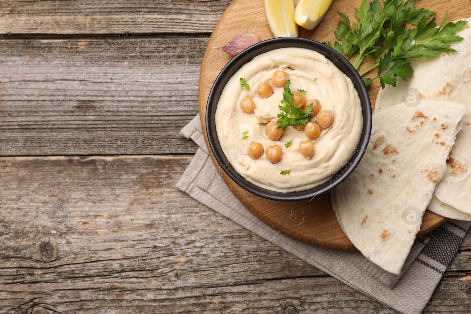 Photo of Delicious hummus with chickpeas and pita served on wooden table, flat lay. Space for text