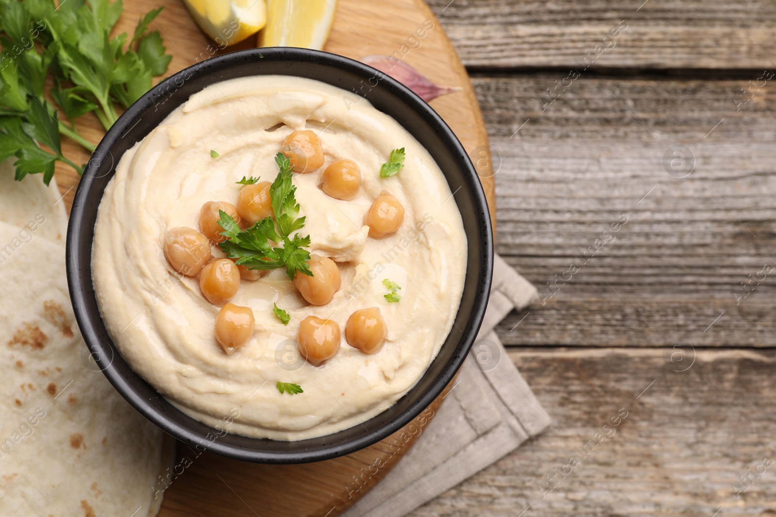 Photo of Delicious hummus with chickpeas and pita served on wooden table, flat lay. Space for text