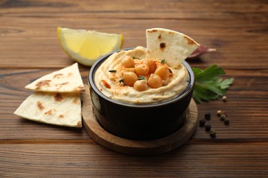 Photo of Delicious hummus with chickpeas and pita served on wooden table