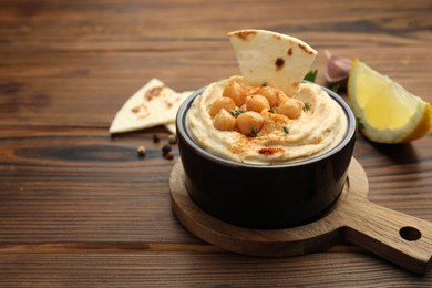 Photo of Delicious hummus with chickpeas and pita served on wooden table, space for text