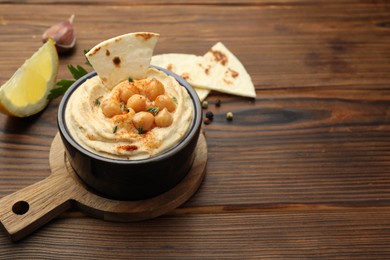 Photo of Delicious hummus with chickpeas and pita served on wooden table, space for text