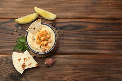 Photo of Delicious hummus with chickpeas and pita served on wooden table, flat lay. Space for text