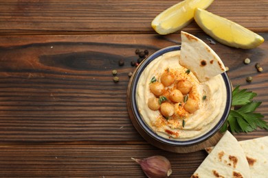 Photo of Delicious hummus with chickpeas and pita served on wooden table, flat lay. Space for text