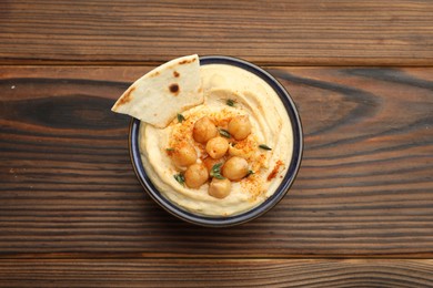 Photo of Delicious hummus with chickpeas and pita served on wooden table, top view