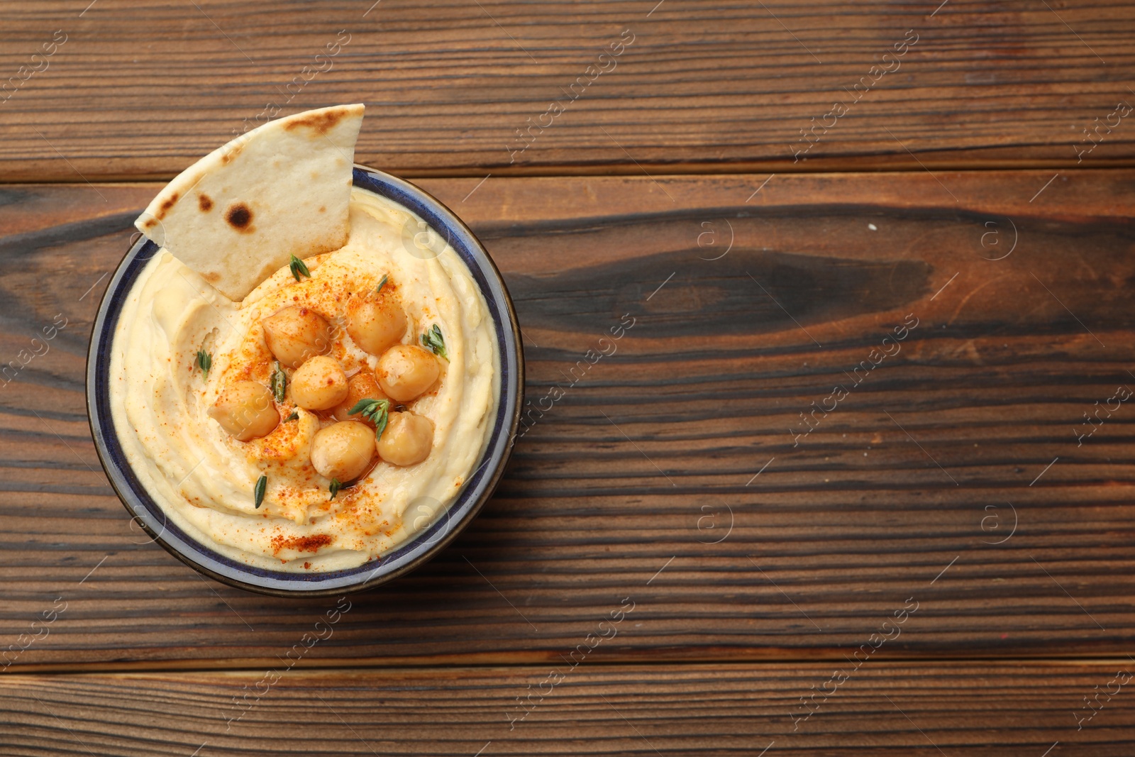 Photo of Delicious hummus with chickpeas and pita served on wooden table, top view. Space for text