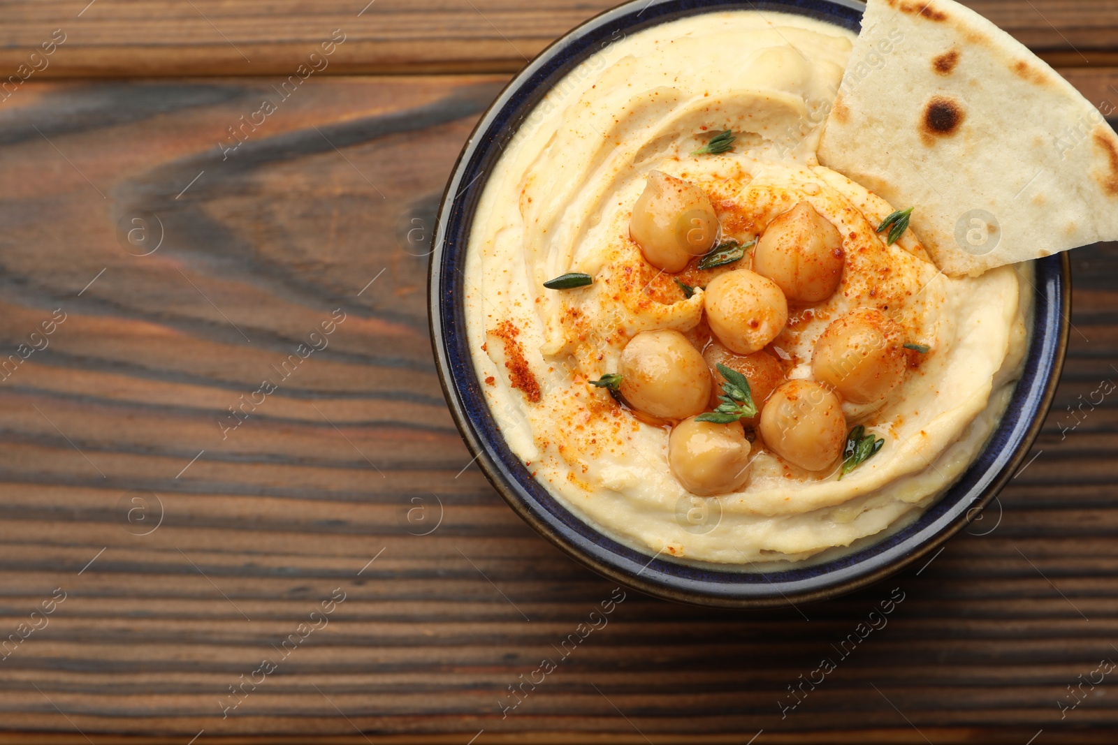 Photo of Delicious hummus with chickpeas and pita served on wooden table, top view. Space for text