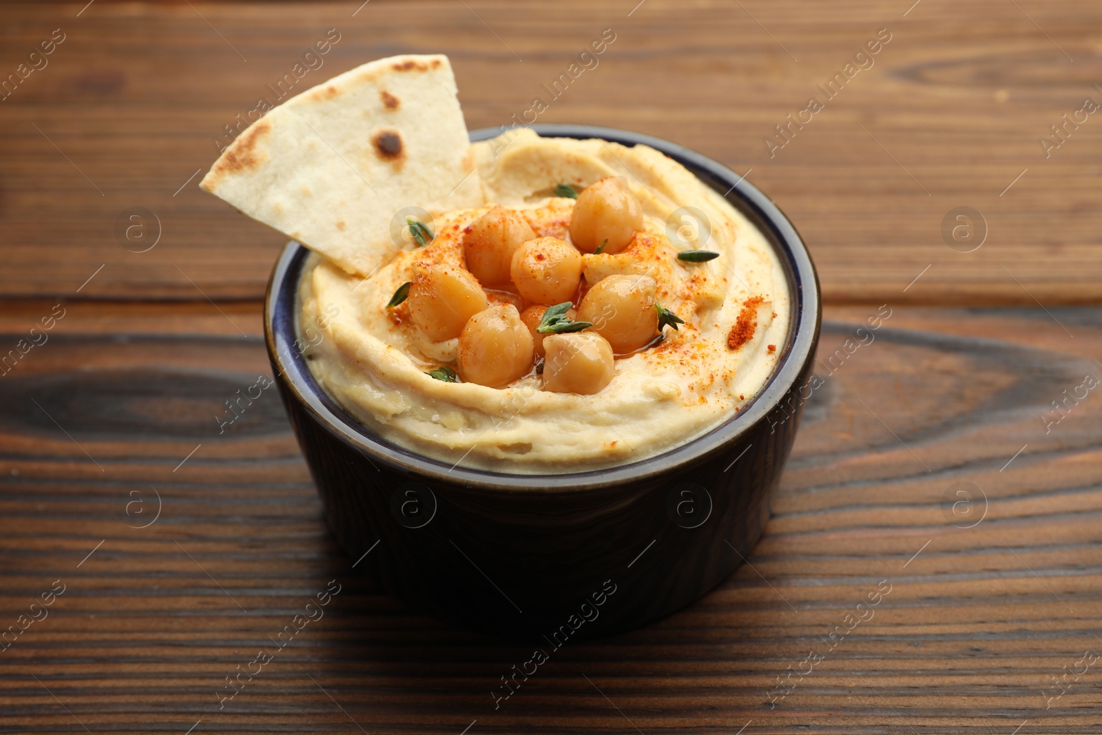 Photo of Delicious hummus with chickpeas and pita served on wooden table