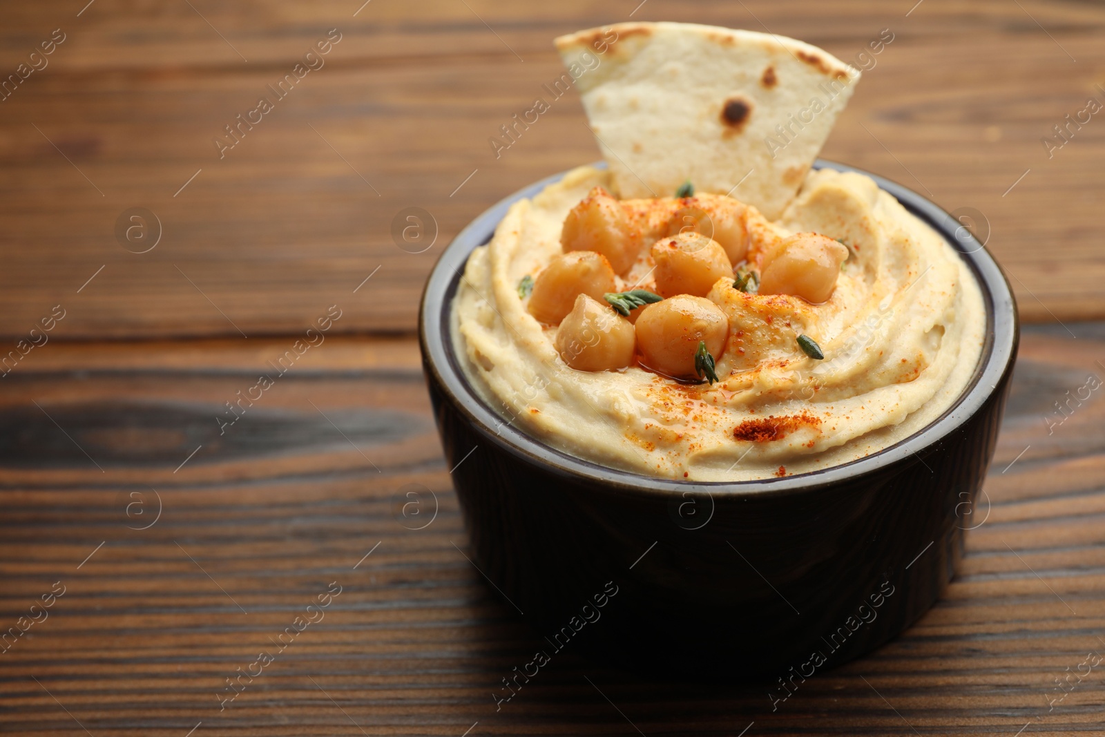 Photo of Delicious hummus with chickpeas and pita served on wooden table, space for text