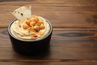 Photo of Delicious hummus with chickpeas and pita served on wooden table, space for text