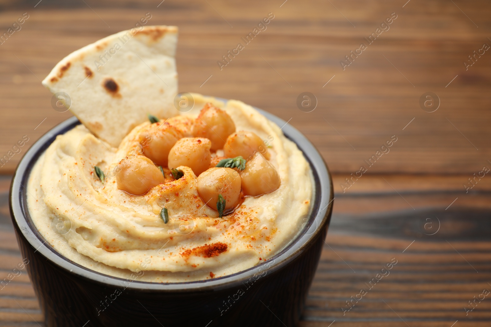 Photo of Delicious hummus with chickpeas and pita served on wooden table, closeup. Space for text