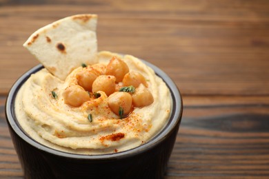 Photo of Delicious hummus with chickpeas and pita served on wooden table, closeup. Space for text