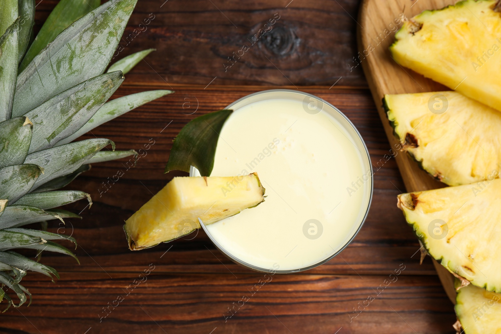 Photo of Tasty pineapple smoothie in glass, leaves and slices of fruit on wooden table, flat lay