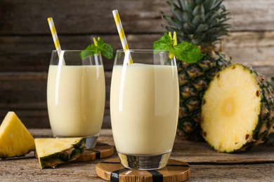 Photo of Tasty pineapple smoothie in glasses, mint and fruit on wooden table, closeup