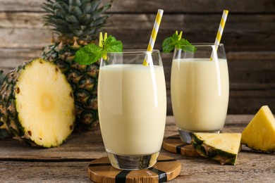 Photo of Tasty pineapple smoothie in glasses, mint and fruit on wooden table, closeup