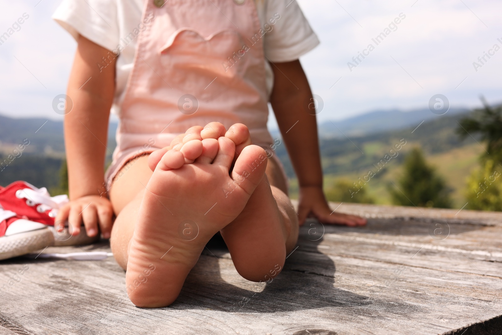 Photo of Little girl sitting on wooden deck outdoors, closeup