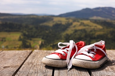 Photo of Pair of red shoes on wooden surface in mountains, space for text