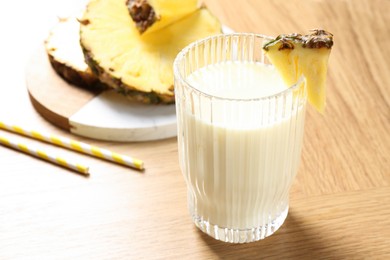 Photo of Tasty pineapple smoothie in glass and fresh fruit on wooden table, closeup