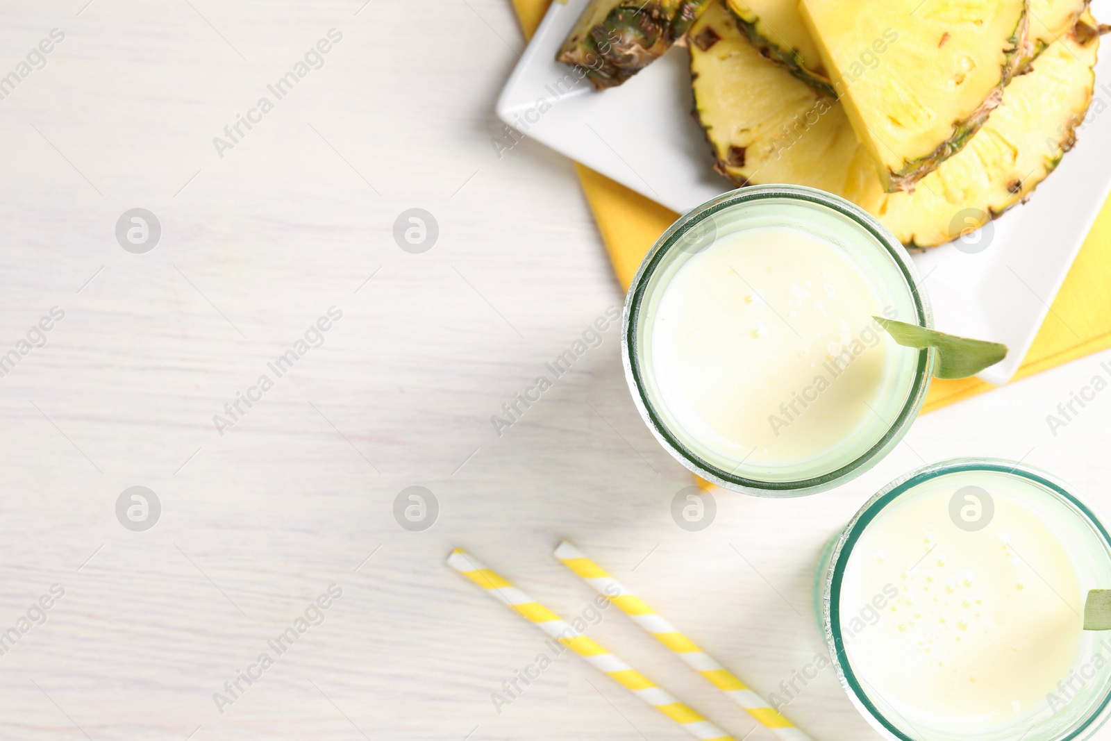 Photo of Tasty pineapple smoothie in glasses and fresh fruit on white wooden table, top view. Space for text