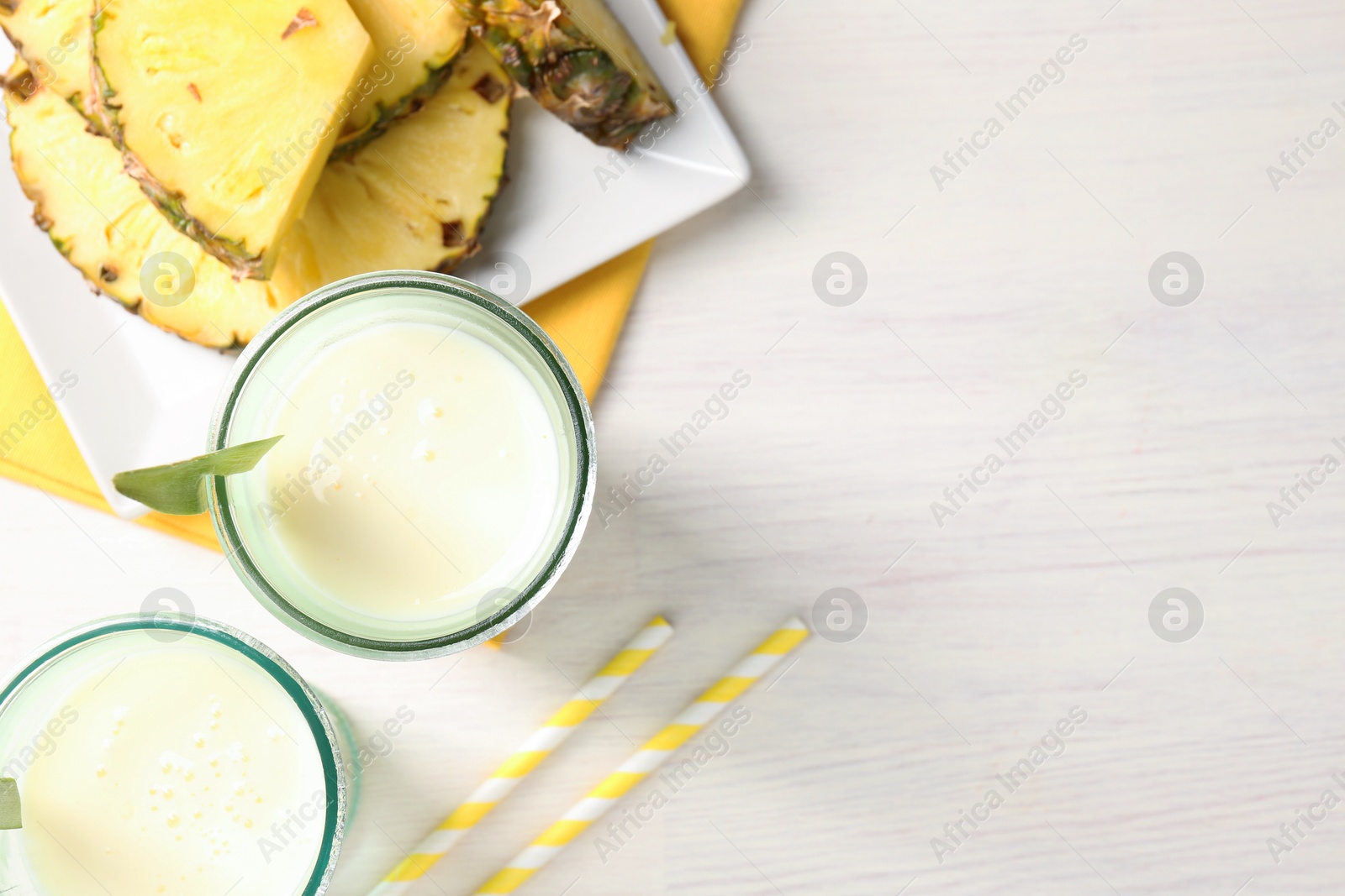 Photo of Tasty pineapple smoothie in glasses and fresh fruit on white wooden table, top view. Space for text