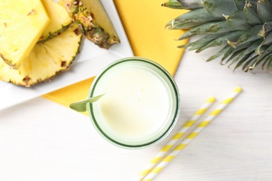 Photo of Tasty pineapple smoothie in glass and fresh fruit on white wooden table, top view