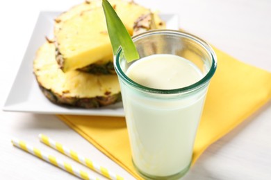 Photo of Tasty pineapple smoothie in glass and fresh fruit on white table, closeup