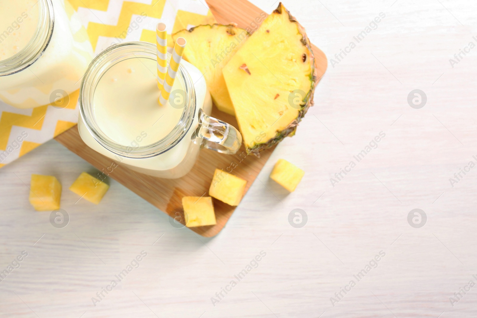 Photo of Tasty pineapple smoothie in mason jars and fresh fruit on white wooden table, top view. Space for text