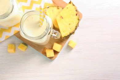 Photo of Tasty pineapple smoothie in mason jars and fresh fruit on white wooden table, top view. Space for text