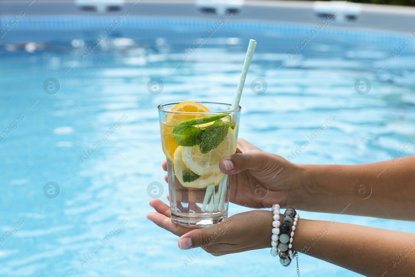 Photo of Woman holding tasty cocktail in glass near swimming pool outdoors, closeup