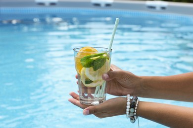 Photo of Woman holding tasty cocktail in glass near swimming pool outdoors, closeup