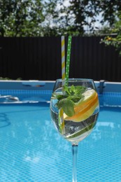 Photo of Tasty cocktail in glass near swimming pool outdoors