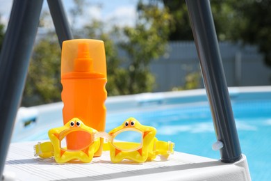 Photo of Bottle of sunscreen and swim goggles near swimming pool outdoors, space for text